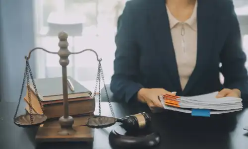 A social security disability lawyer holding a stack of documents from behind her desk.